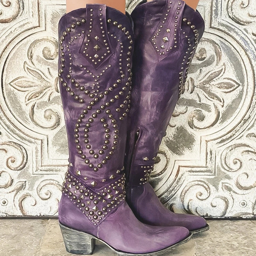 Purple cowboy boots with gold studs on a decorative wall background