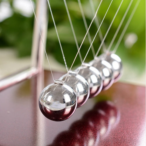Newton's cradle with silver balls on a blurred green background