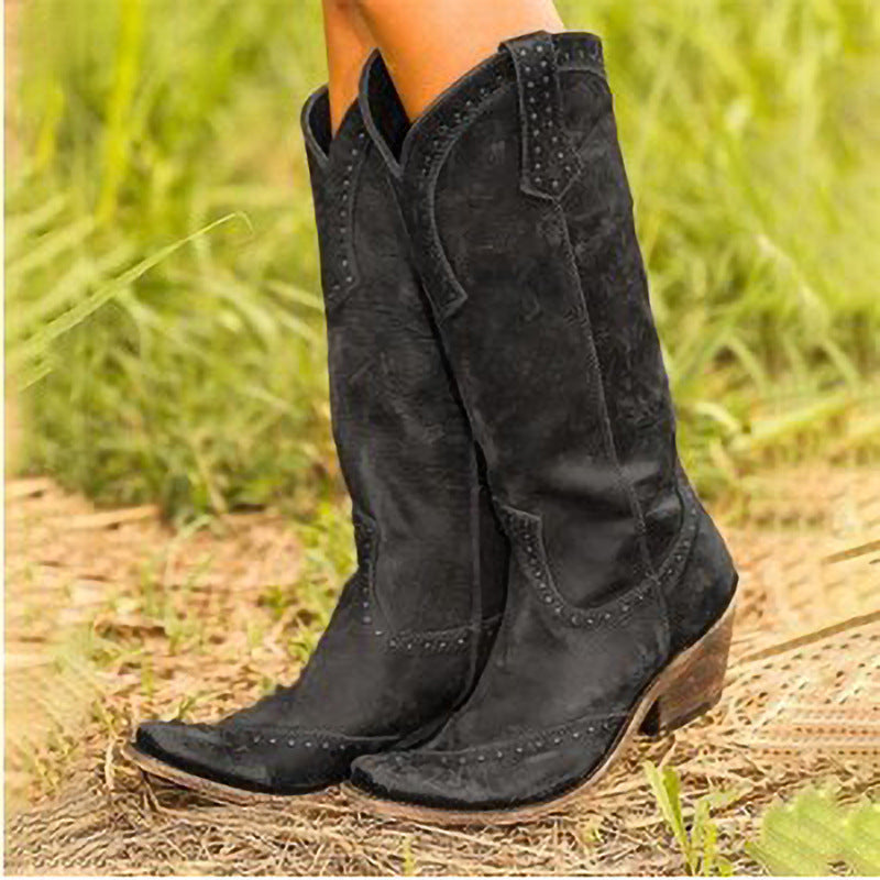 Black cowboy boots worn by a person standing on grass.