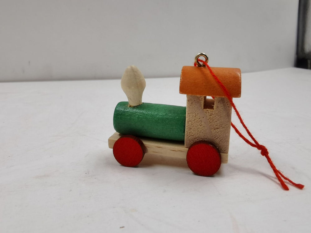Small wooden toy train with a green body, red wheels, and an orange roof on a white surface.