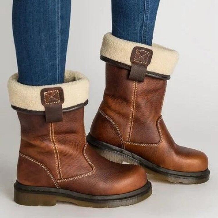 Brown leather boots with white fur lining worn with blue jeans on a light gray background