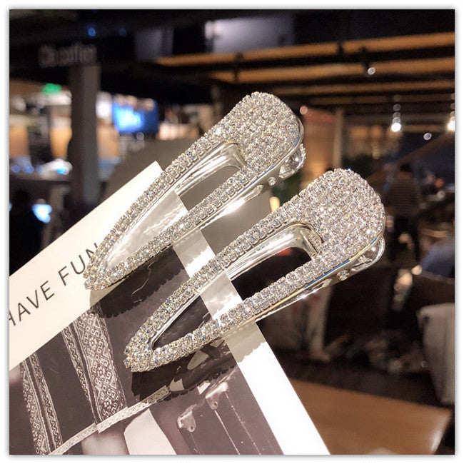 Two silver hair clips with rhinestones on a blurred indoor background