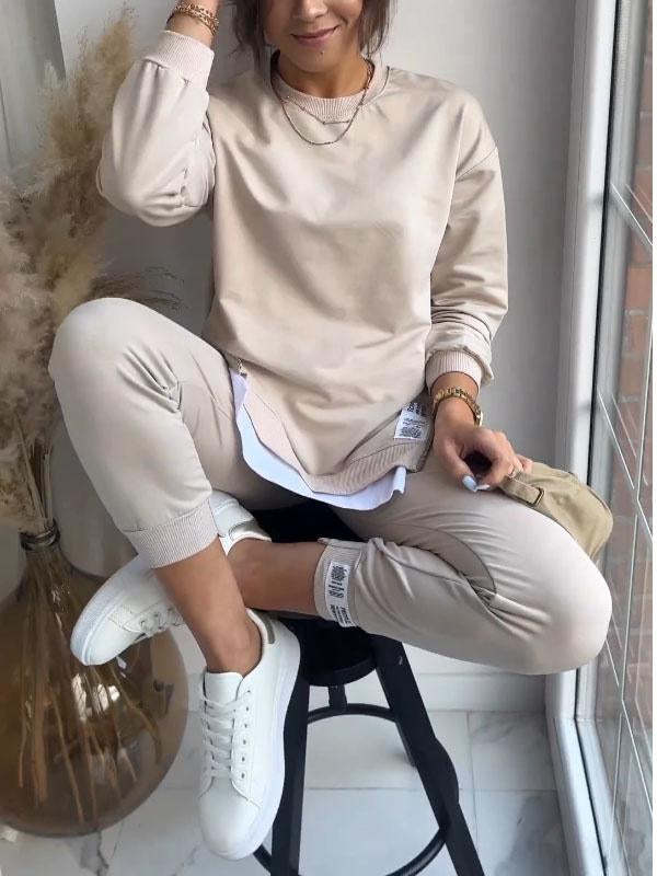 Person wearing a beige sweatshirt and pants sitting on a stool indoors.