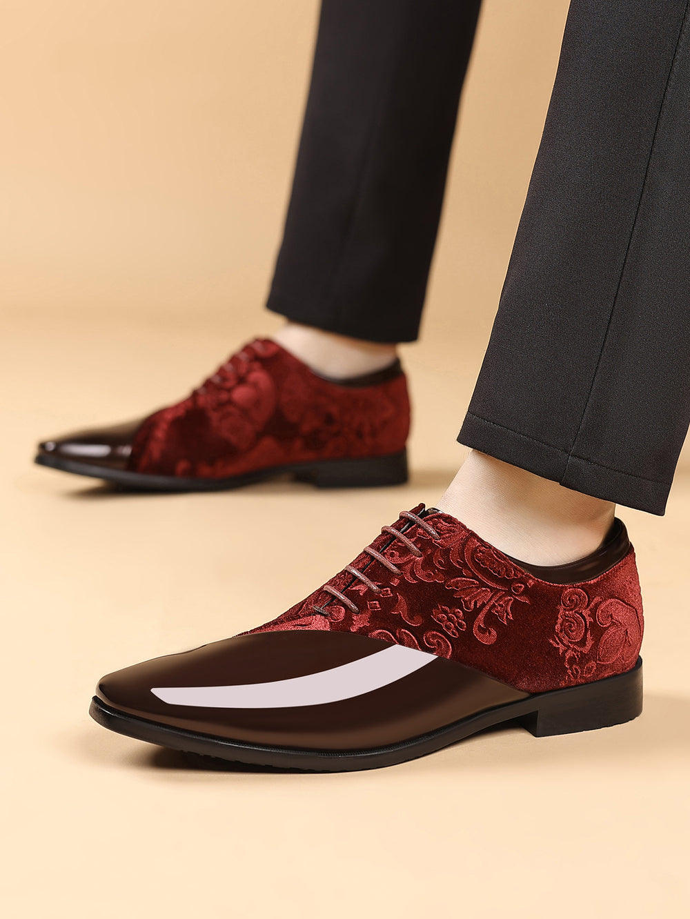 Red and black patterned dress shoes worn with dark pants on a beige background