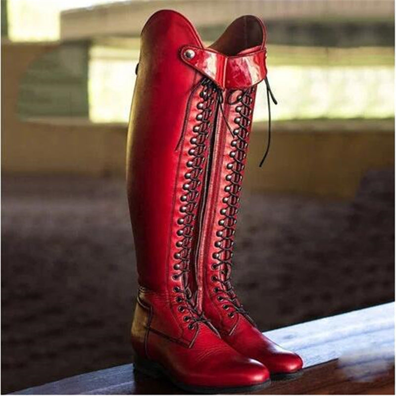 Red leather knee-high boots with detailed laces on a wooden surface.