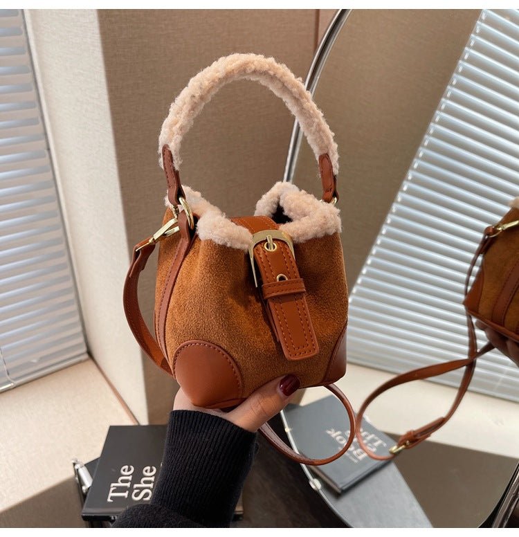 Brown suede handbag with fur trim held by a hand against a neutral background