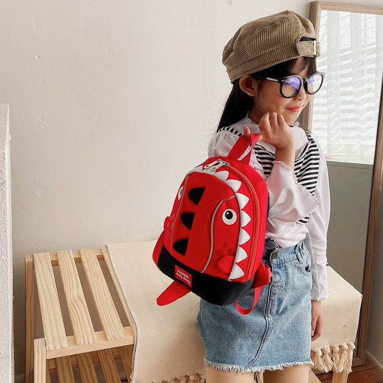 Child wearing a red dinosaur backpack indoors