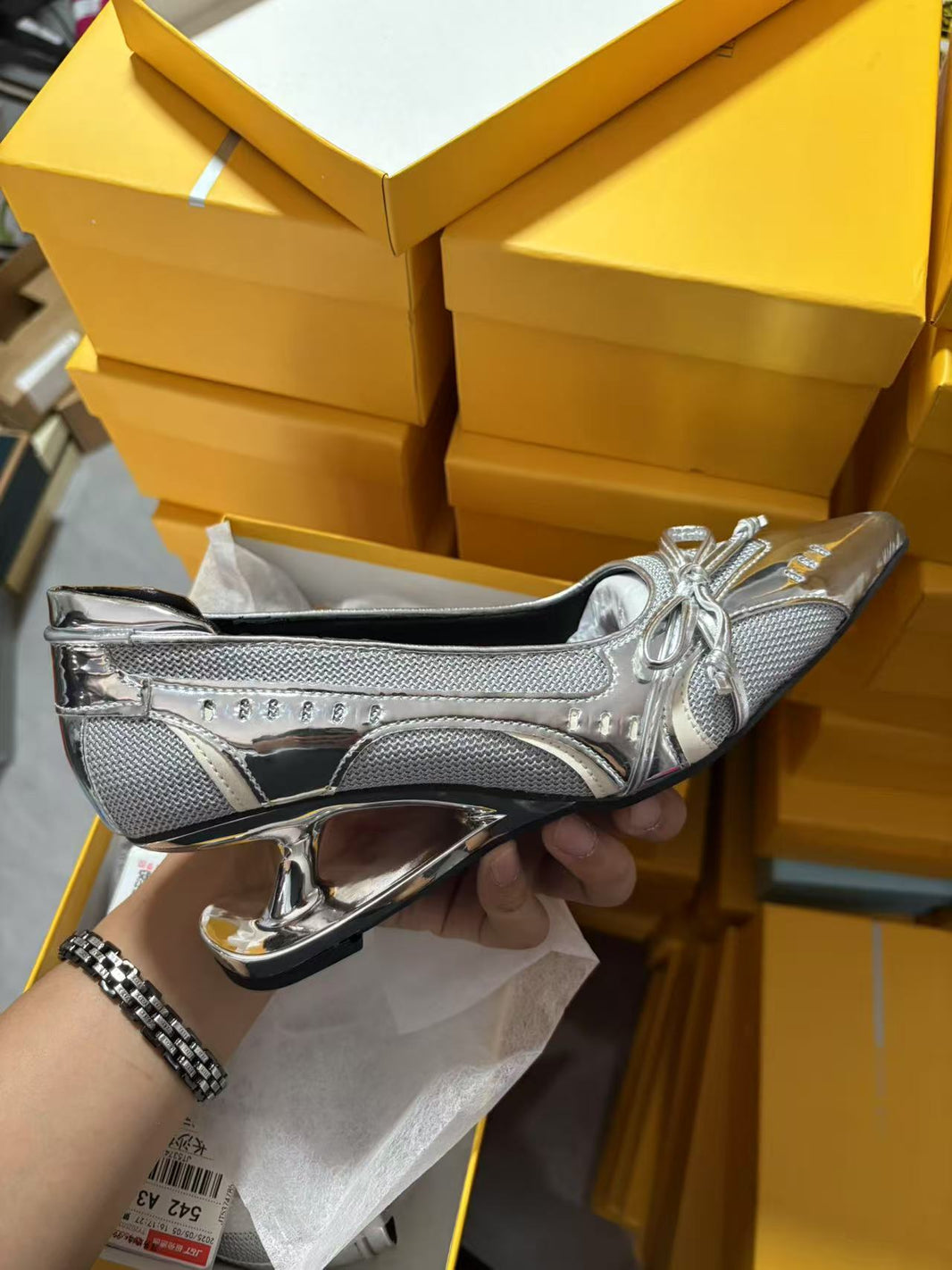 Silver high-heeled shoe held by a hand with yellow boxes in the background