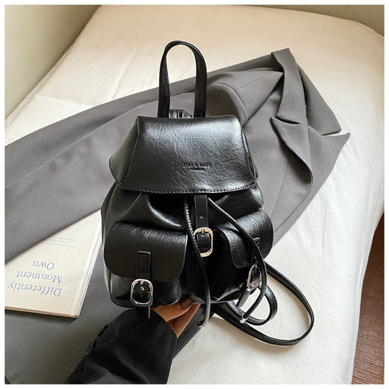 Black leather backpack held by a hand on a light-colored surface with a gray fabric background.