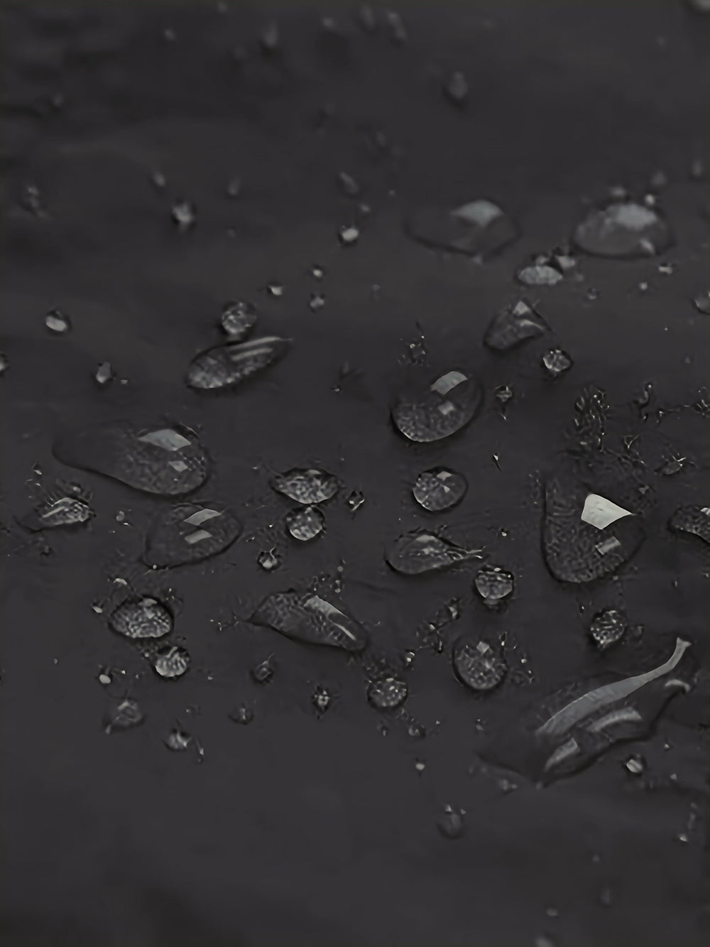 Close-up of water droplets resting on a dark, matte, waterproof surface.