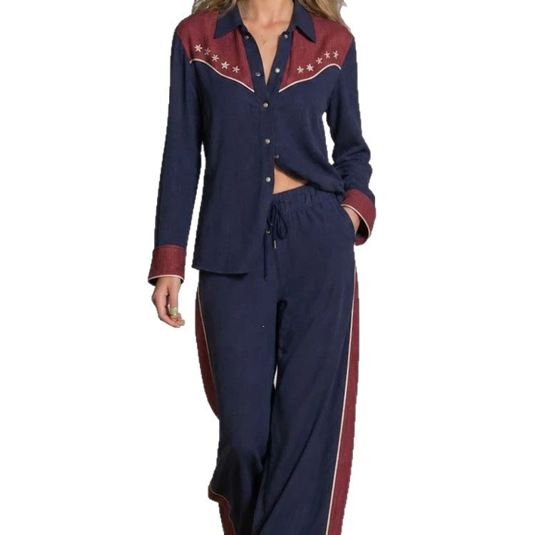 A woman wearing a matching navy blue two-piece lounge set with burgundy and white western-style embroidery on the shirt and red side panels on the pants, shown against a plain white background.