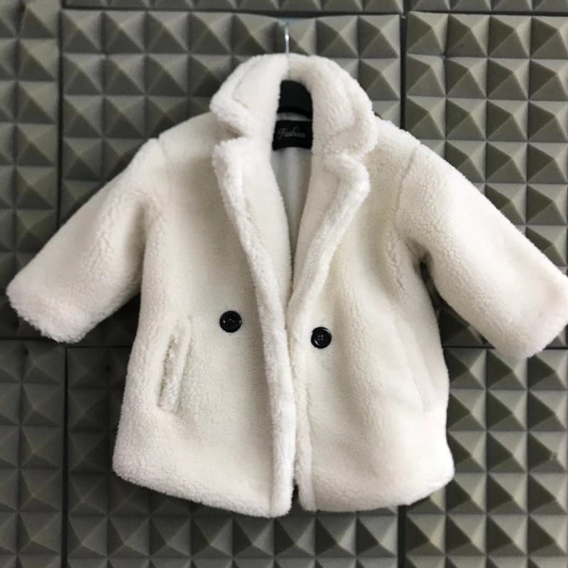 White fluffy coat with black buttons on a hanger against a geometric patterned wall.