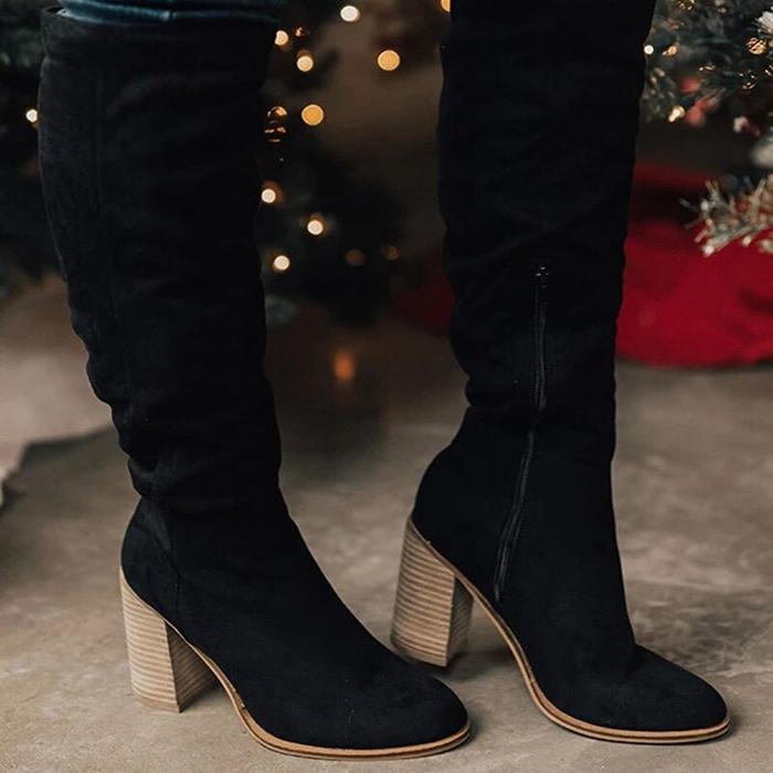 Black knee-high boots with wooden block heels worn indoors with blurred festive background