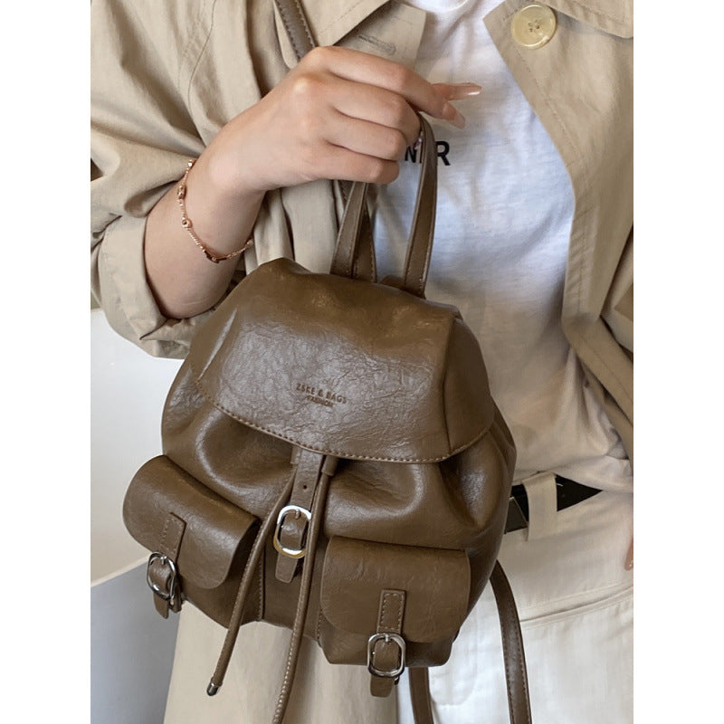 Brown leather backpack held by a person wearing a beige trench coat.