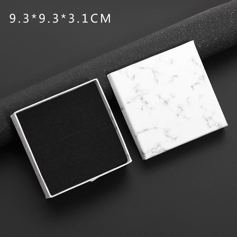 Two square boxes, one black and one with a white marble pattern, on a dark surface.