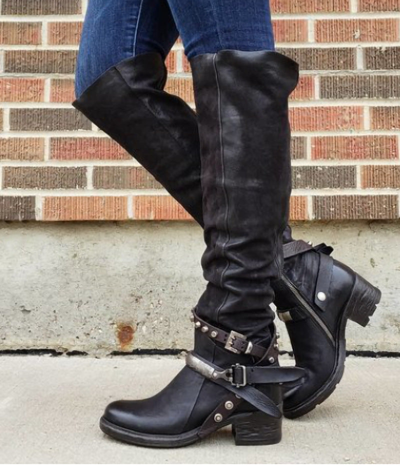 Black leather boots with buckles worn by a person against a brick wall.