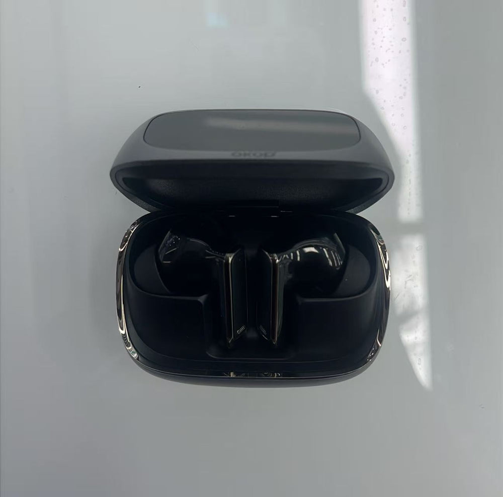 Open black wireless earbuds charging case with the earbuds inside, photographed from above on a glossy white surface with soft window light reflections.