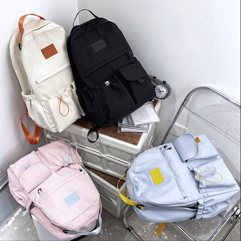 Four backpacks in different colors on a metal cart against a white wall.