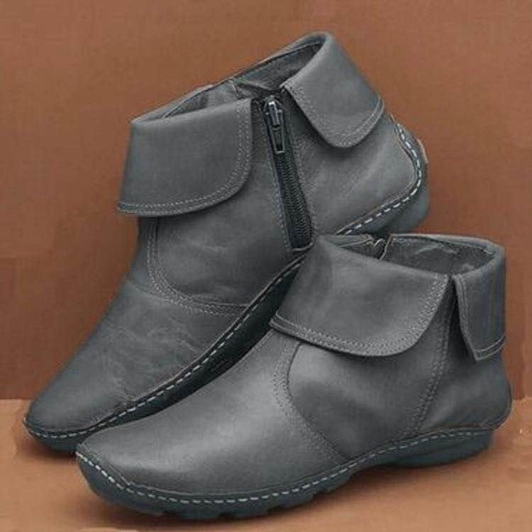 Pair of gray ankle boots with a zipper on a brown background