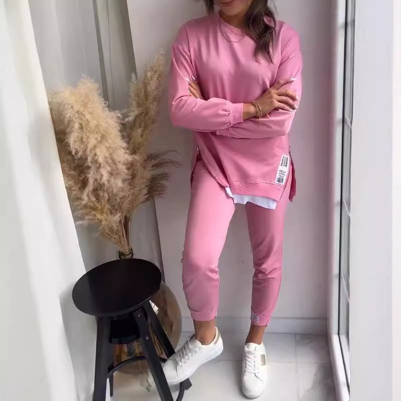 Person wearing a pink outfit standing in a room with a black stool and dried plants.