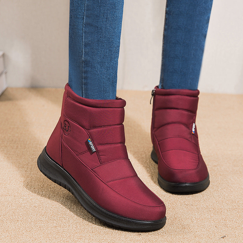 Red winter boots worn with blue jeans on a beige floor.