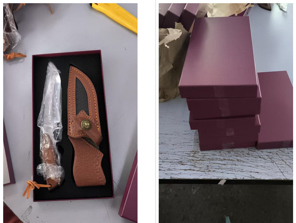 Knife with sheath in a box on a gray surface, next to stacked purple boxes.