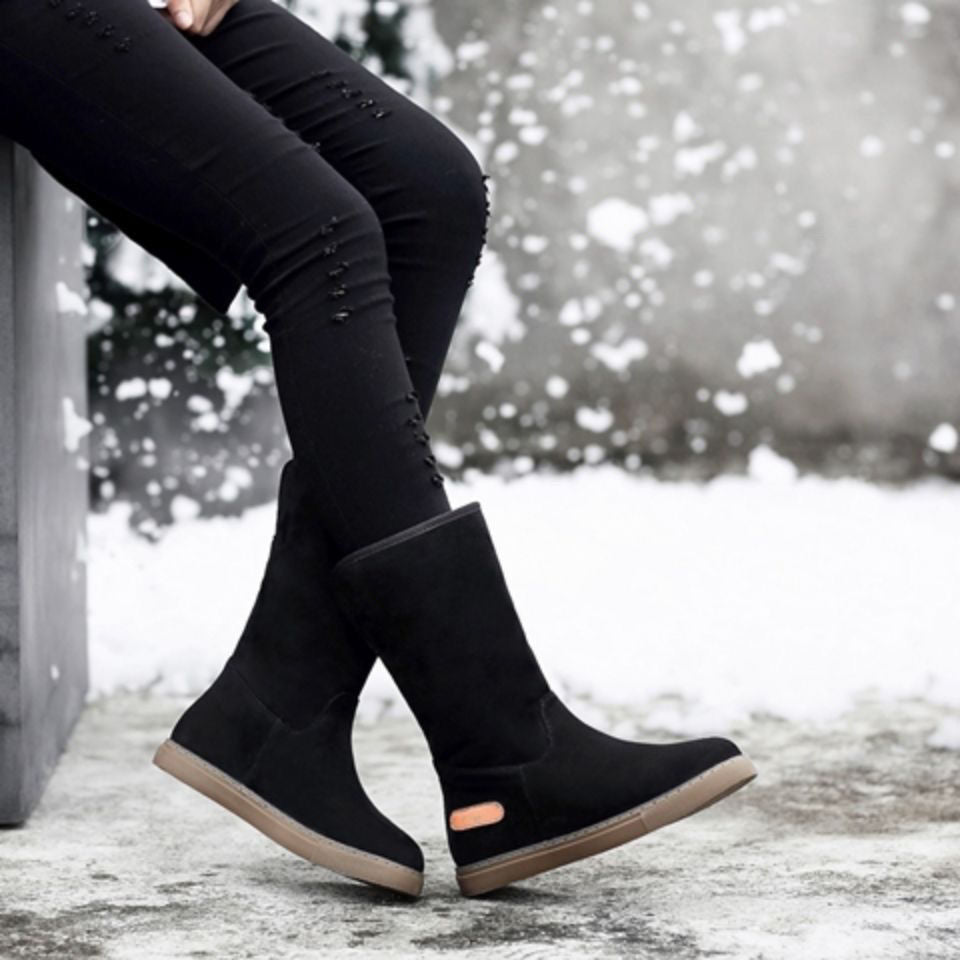 Black knee-high boots worn with black pants in a snowy outdoor setting
