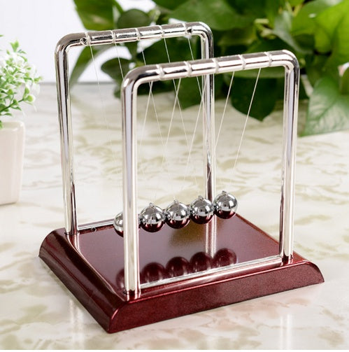 Newton's cradle on a wooden base with a blurred green plant background