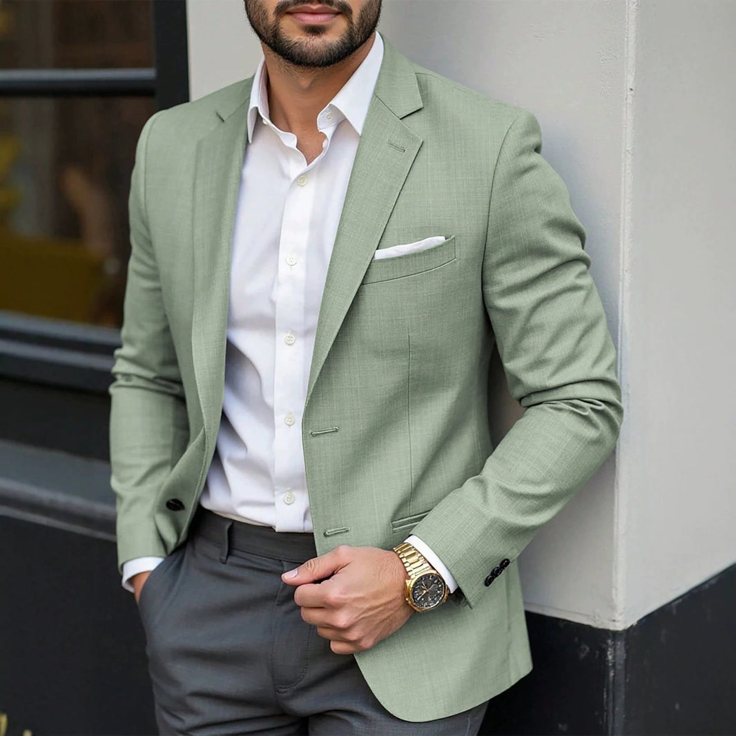 Man wearing a light green blazer over a white shirt with gray pants, standing against a neutral background.