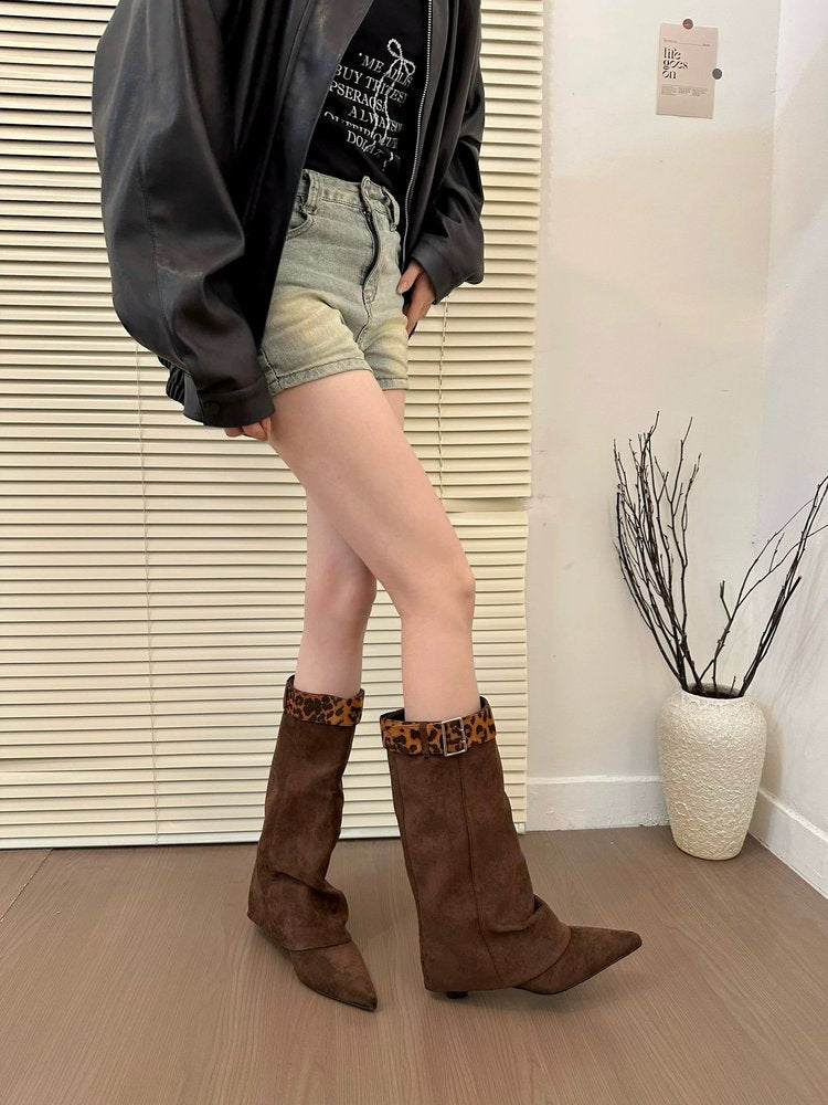 Person wearing brown knee-high boots with leopard print trim in a room with a plant and window blinds.