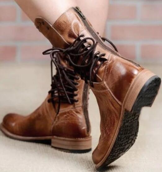 Brown leather boots with laces worn by a person on a light background