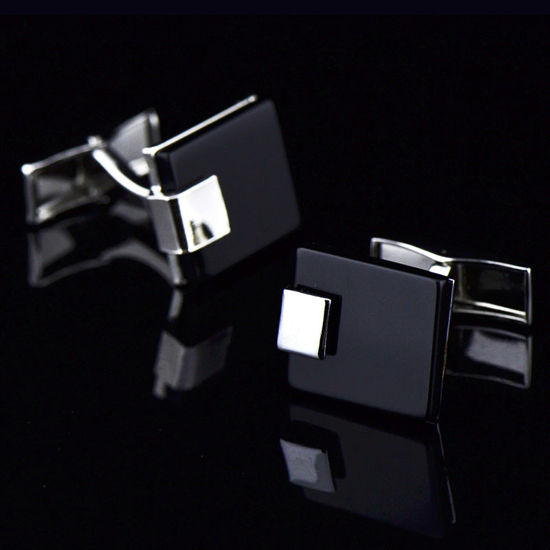 Black and silver square cufflinks on a reflective black surface