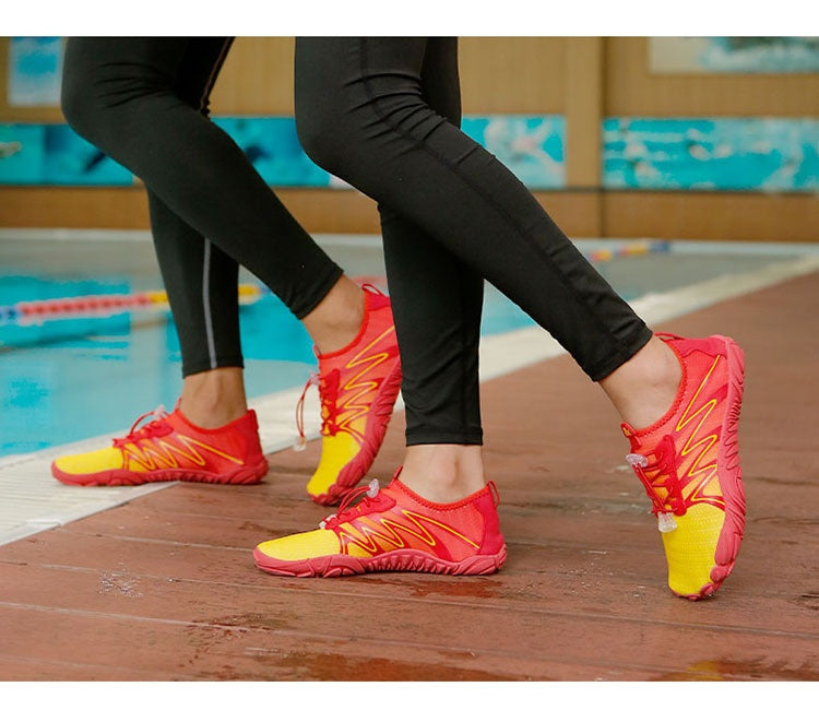 A close-up of a person's legs wearing bright red and yellow athletic water shoes with black leggings, standing on a wet wooden deck next to a swimming pool.