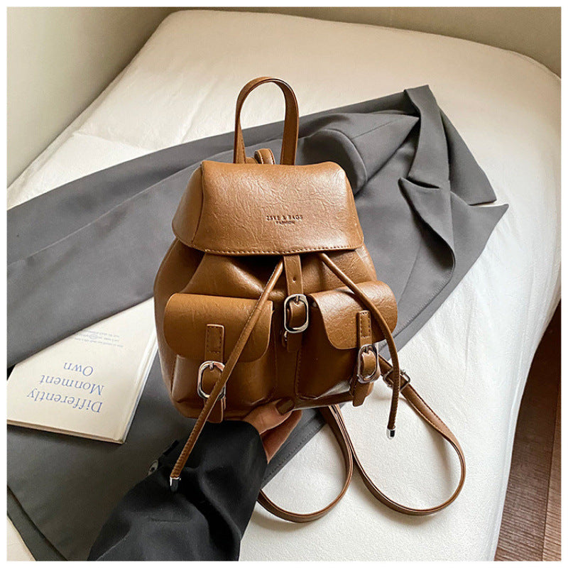Brown leather backpack on a bed with a book and gray fabric