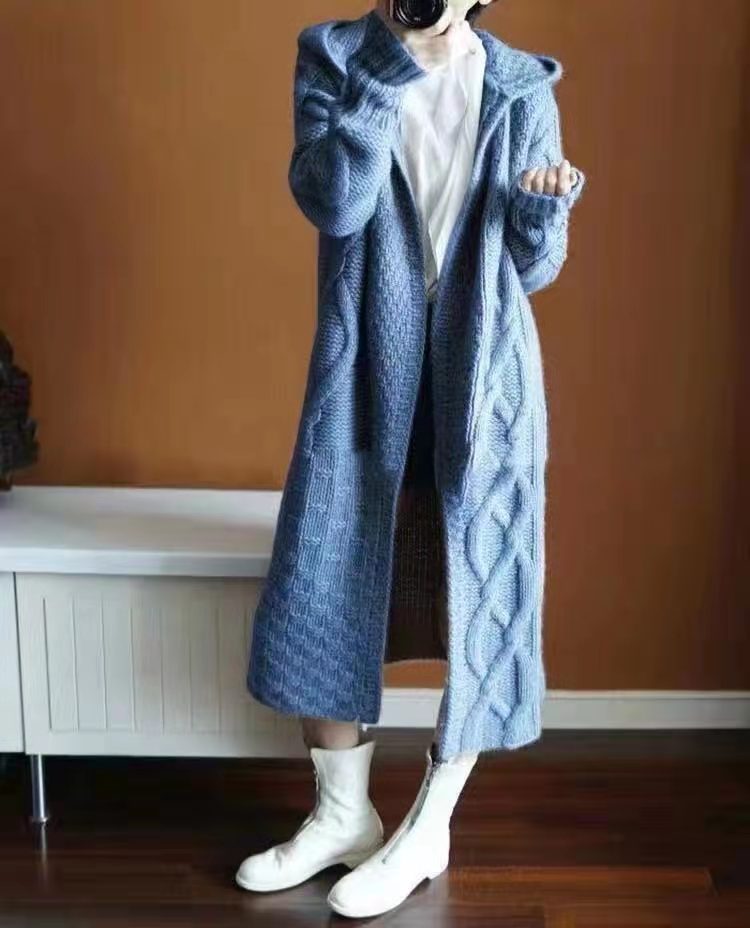 Mannequin wearing a long blue knitted coat against a brown wall.