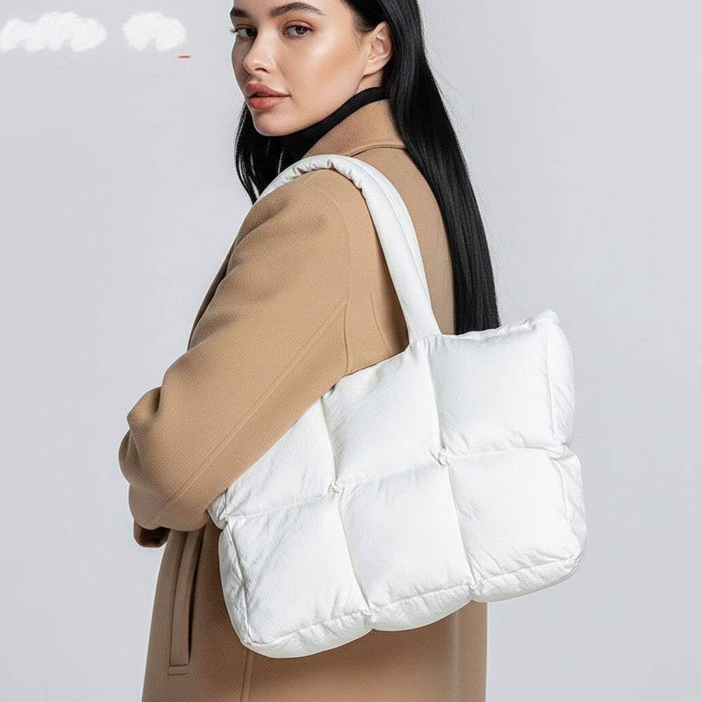 Person holding a white quilted tote bag against a neutral background