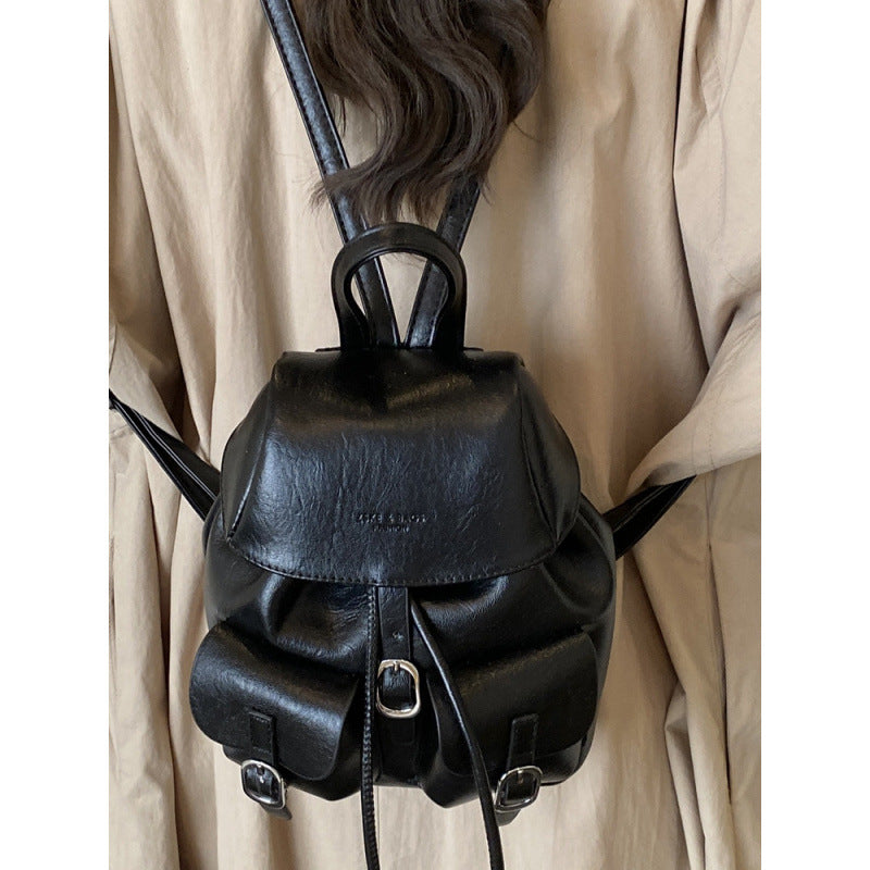 Black leather backpack worn over a beige coat