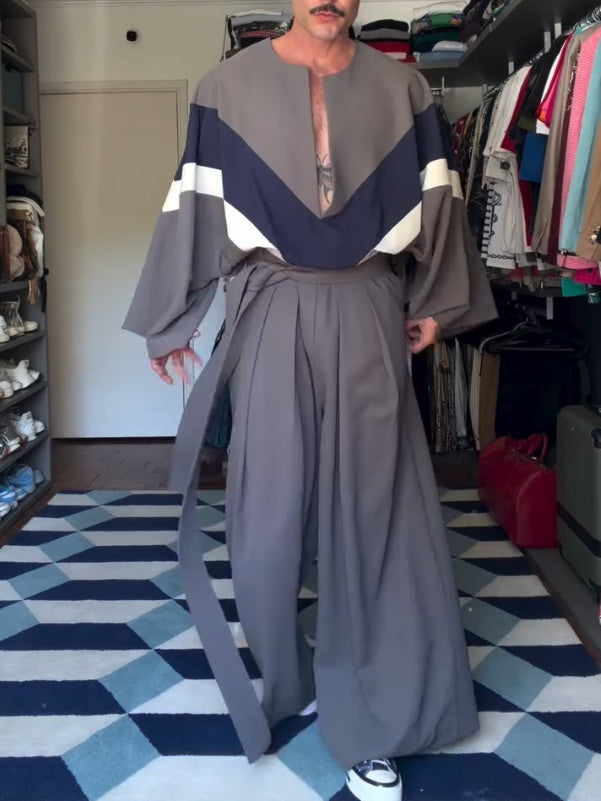 Person wearing a long, gray outfit with geometric patterns in a room with a checkered floor. 2