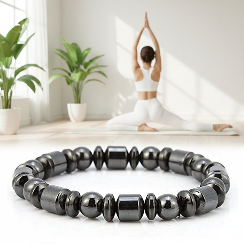 A black beaded bracelet made of polished metallic beads is shown in sharp focus in the foreground, while a woman in white yoga clothing practices in a bright, sunlit room with potted plants in the background.