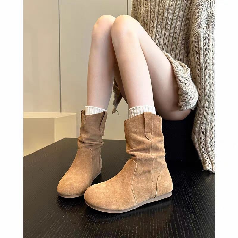 Bottes en daim beige portées par une personne assise sur une surface sombre avec un arrière-plan neutre