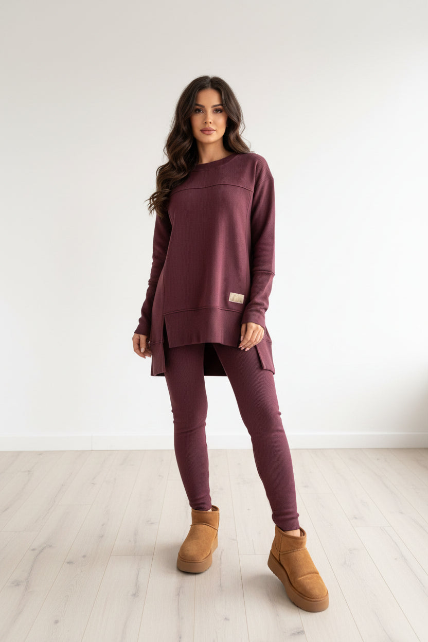Person wearing a maroon outfit with brown boots standing in a modern interior setting.