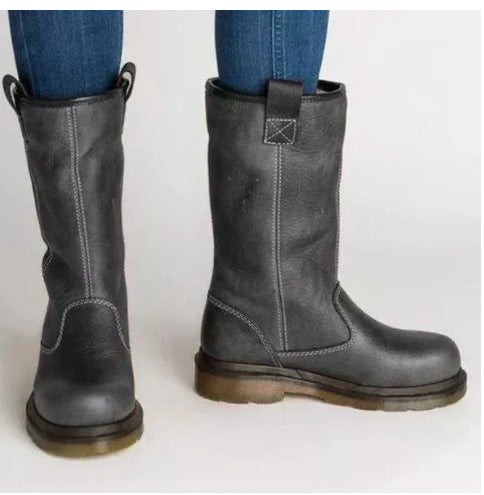 A pair of dark gray leather mid-calf boots with pull tabs and contrast stitching, shown on a person wearing blue jeans against a plain light background.