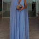 Woman in a blue evening gown with a cape holding a clutch in an indoor setting.