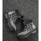 A pair of black high-top lace-up boots with a white bandana print pattern, photographed from a top-down perspective on a dark asphalt surface.