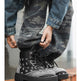 A person wearing black and white patterned lace-up boots with distressed blue denim jeans, sitting on a wooden ledge.