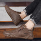 Brown shoes with a brand logo worn by a person on a wooden floor.