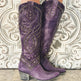 Purple cowboy boots with gold studs on a decorative wall background