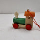 Small wooden toy train with a green body, red wheels, and an orange roof on a white surface.