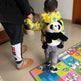 Child in a colorful raincoat with a panda toy, standing on a colorful mat.