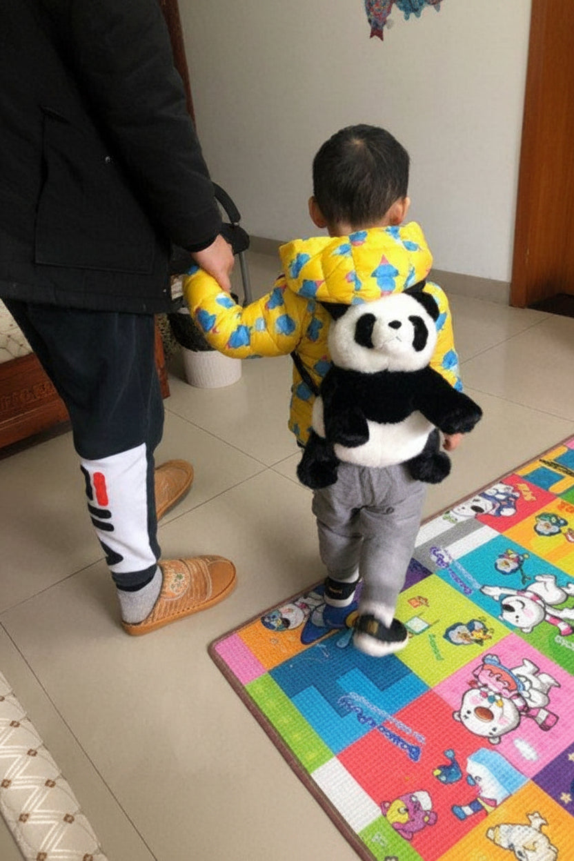 Child in a colorful raincoat with a panda toy, standing on a colorful mat.